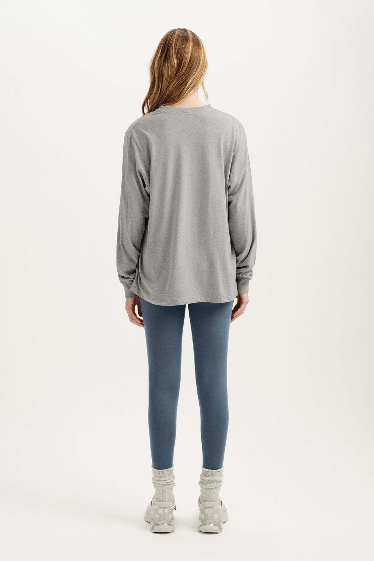 Person wearing a gray long-sleeve top and blue leggings on a white background