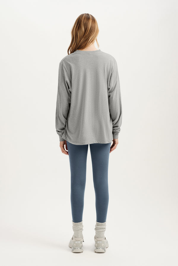 Person wearing a gray long-sleeve top and blue leggings on a white background