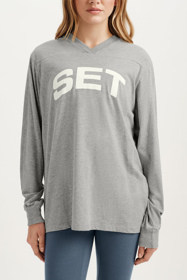 Person wearing a gray long-sleeve shirt with 'SET' printed on it against a white background