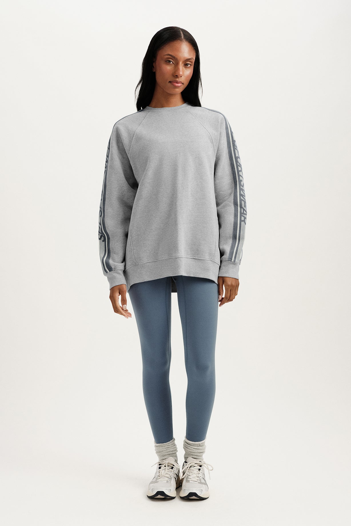 Woman wearing a gray sweatshirt and blue leggings on a white background