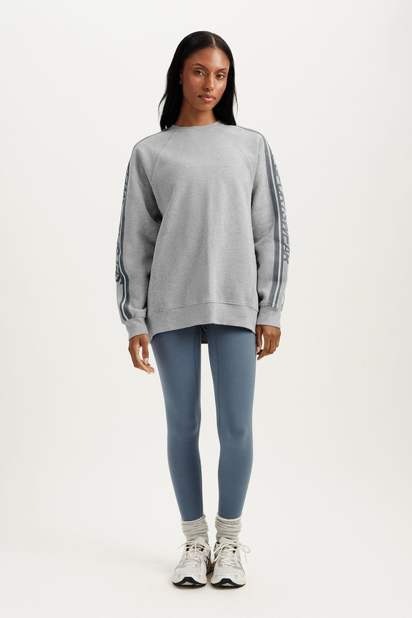 Woman wearing a gray sweatshirt and blue leggings on a white background