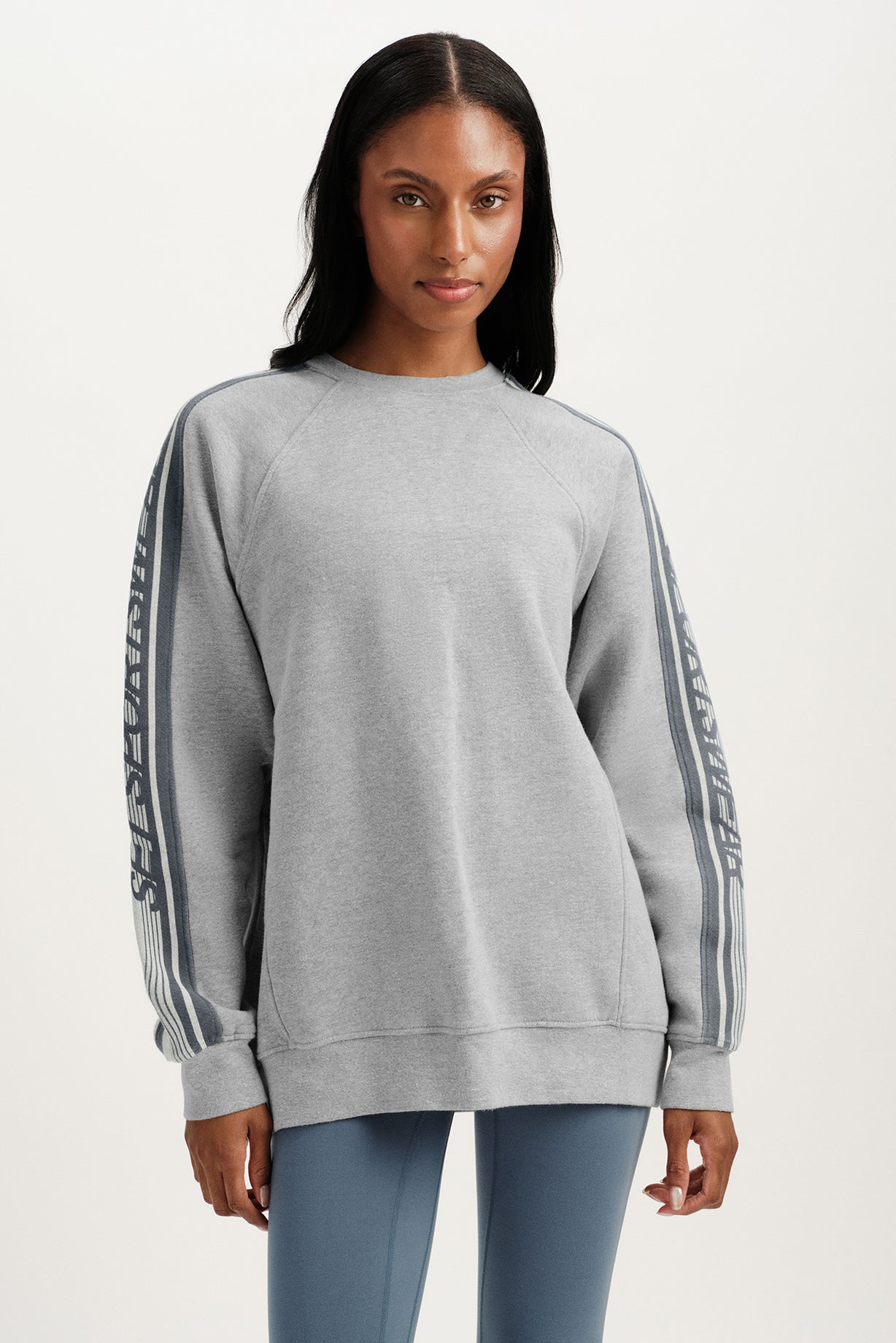 Woman wearing a gray sweatshirt with striped sleeves on a white background <model-info>Sydney wears a size L and is 5’9, 24½” waist, 32B bust.</model-info>