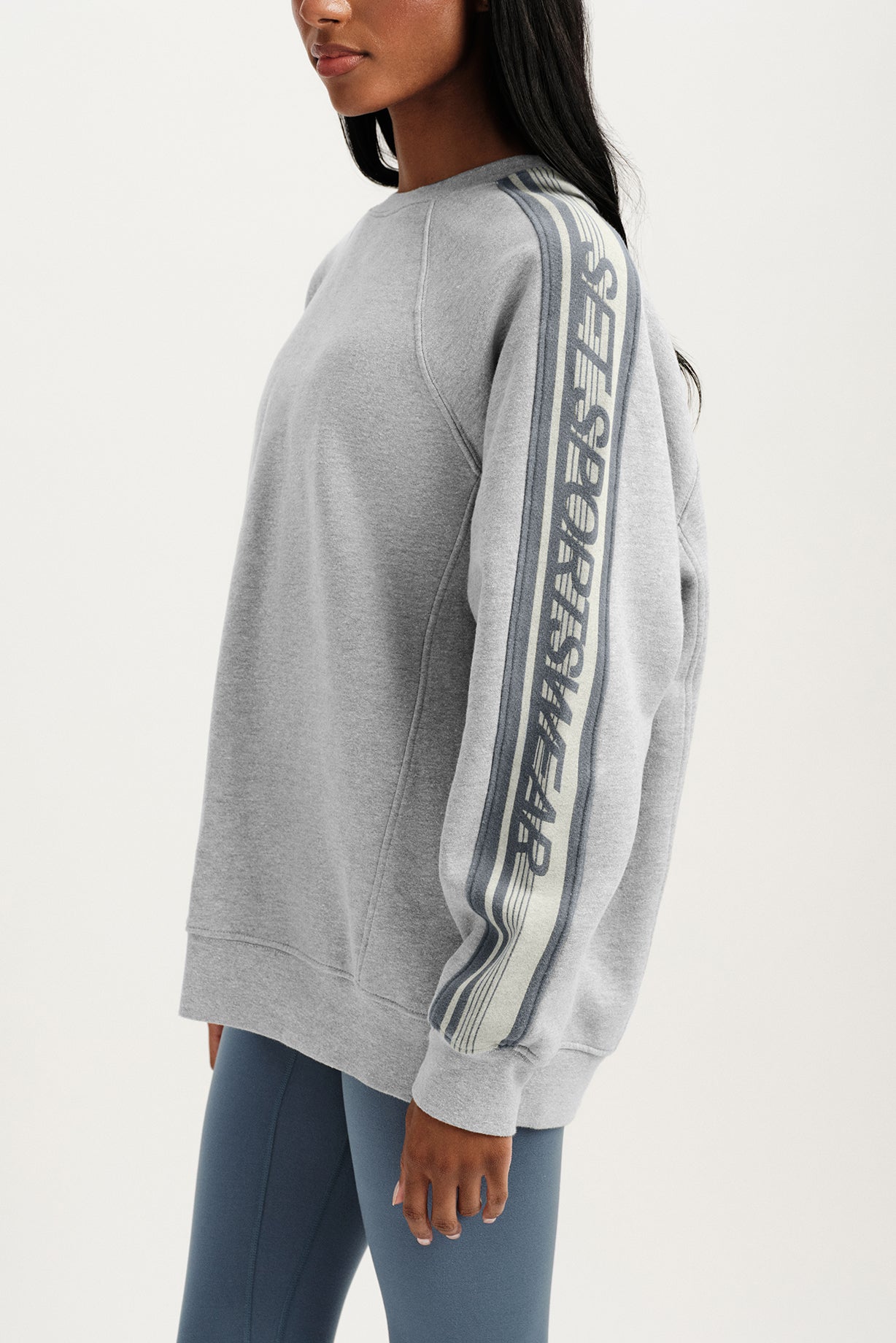 Person wearing a gray sweatshirt with branding on a white background