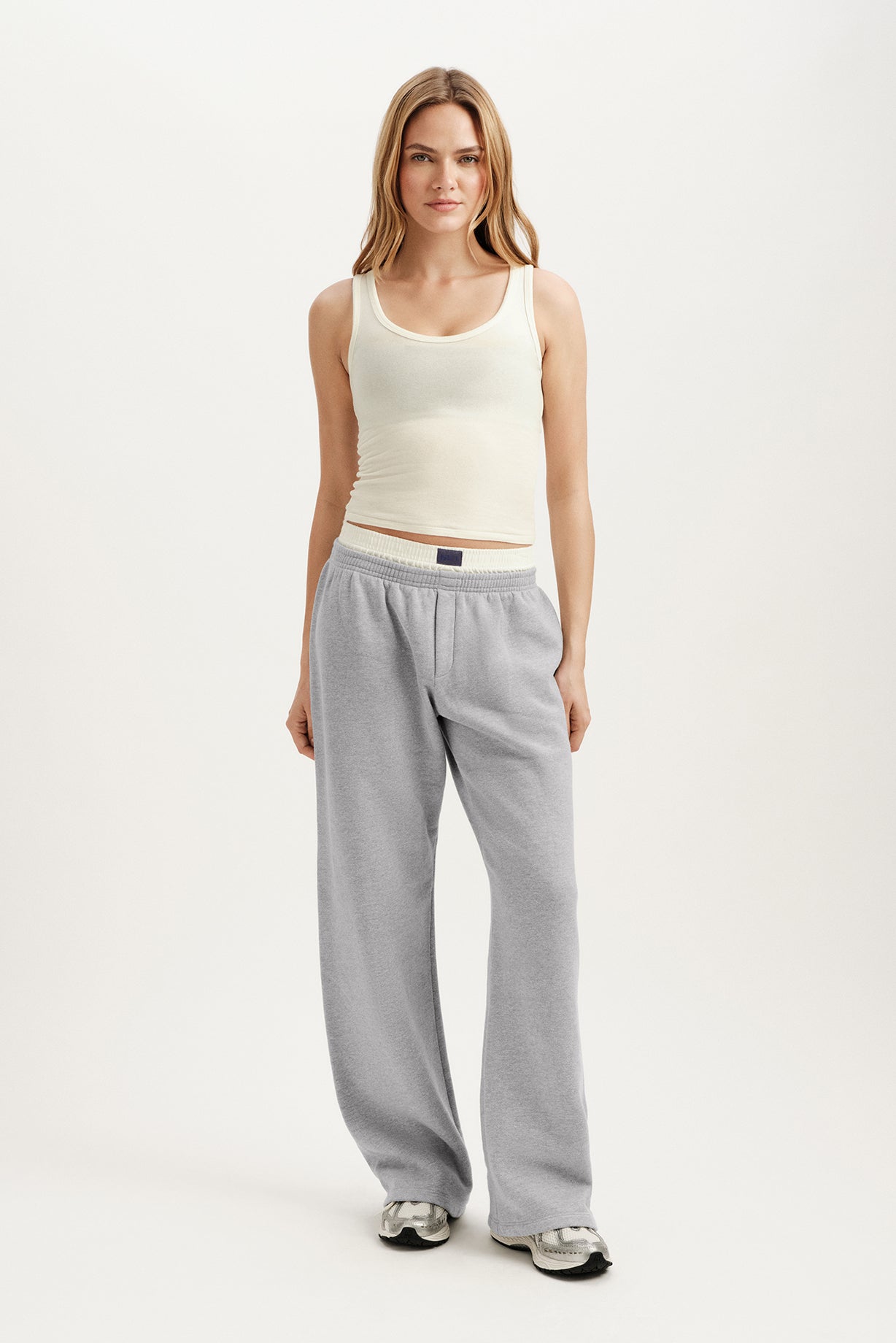 Woman wearing a white tank top and gray pants on a white background