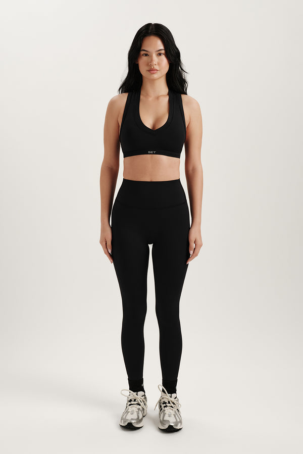 Woman wearing a black sports bra and leggings on a white background