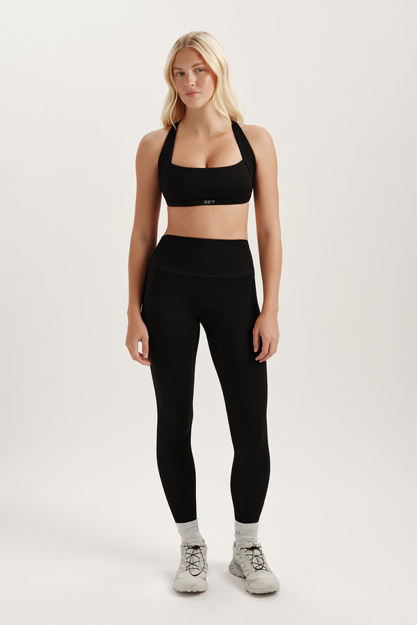 Woman wearing a black sports bra and leggings on a white background