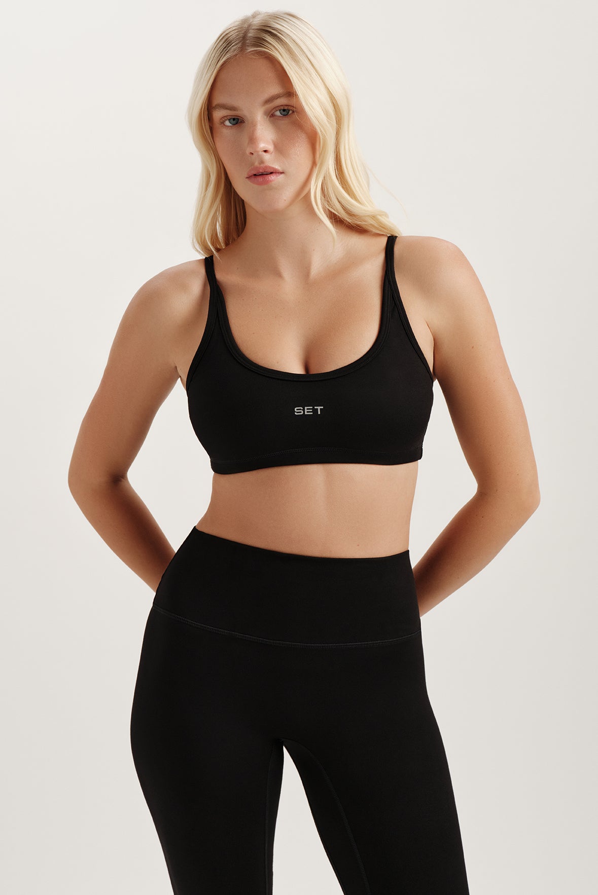 Woman wearing a black sports bra and leggings with a visible brand logo on a light background <model-info>Kenzie wears a size S and is 5’6, 25” waist, 33” bust.</model-info>