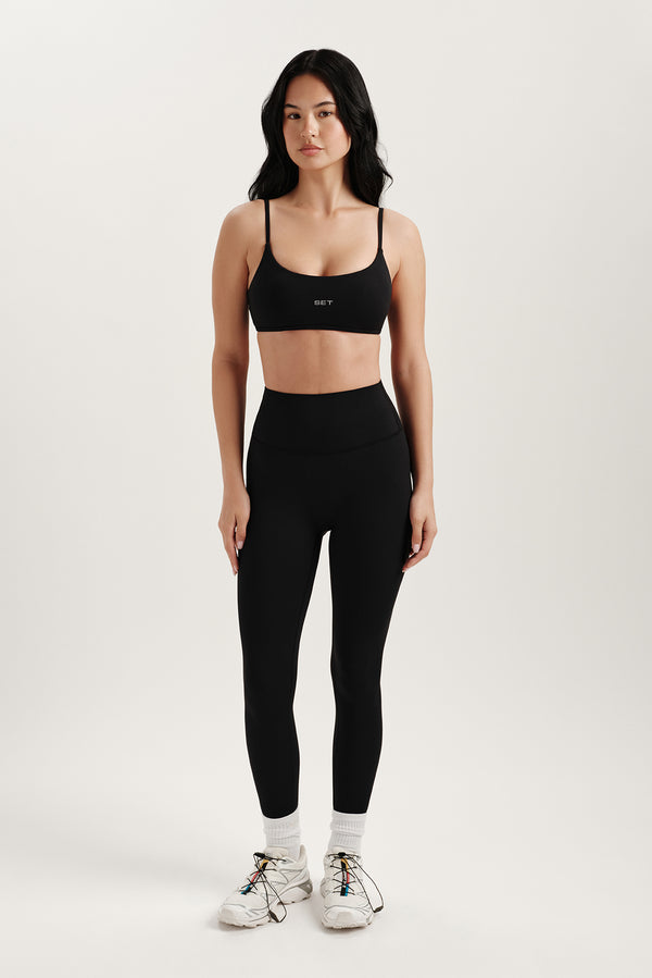 Woman wearing a black sports bra and leggings on a white background