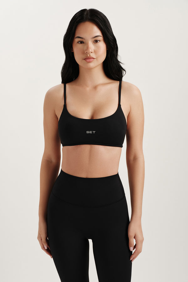 Woman wearing a black sports bra and leggings with 'SET' branding on a light background 