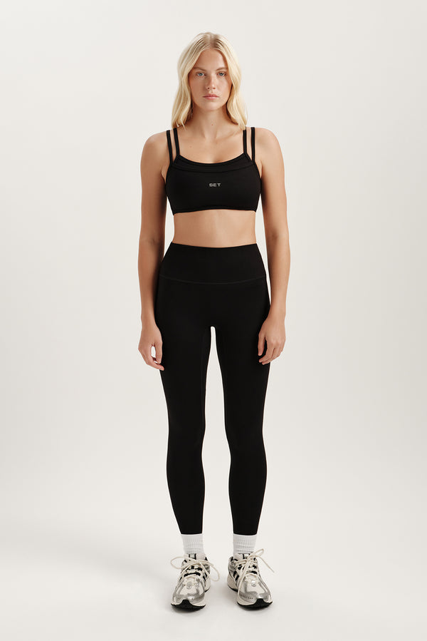 Woman wearing a black sports bra and leggings set on a white background