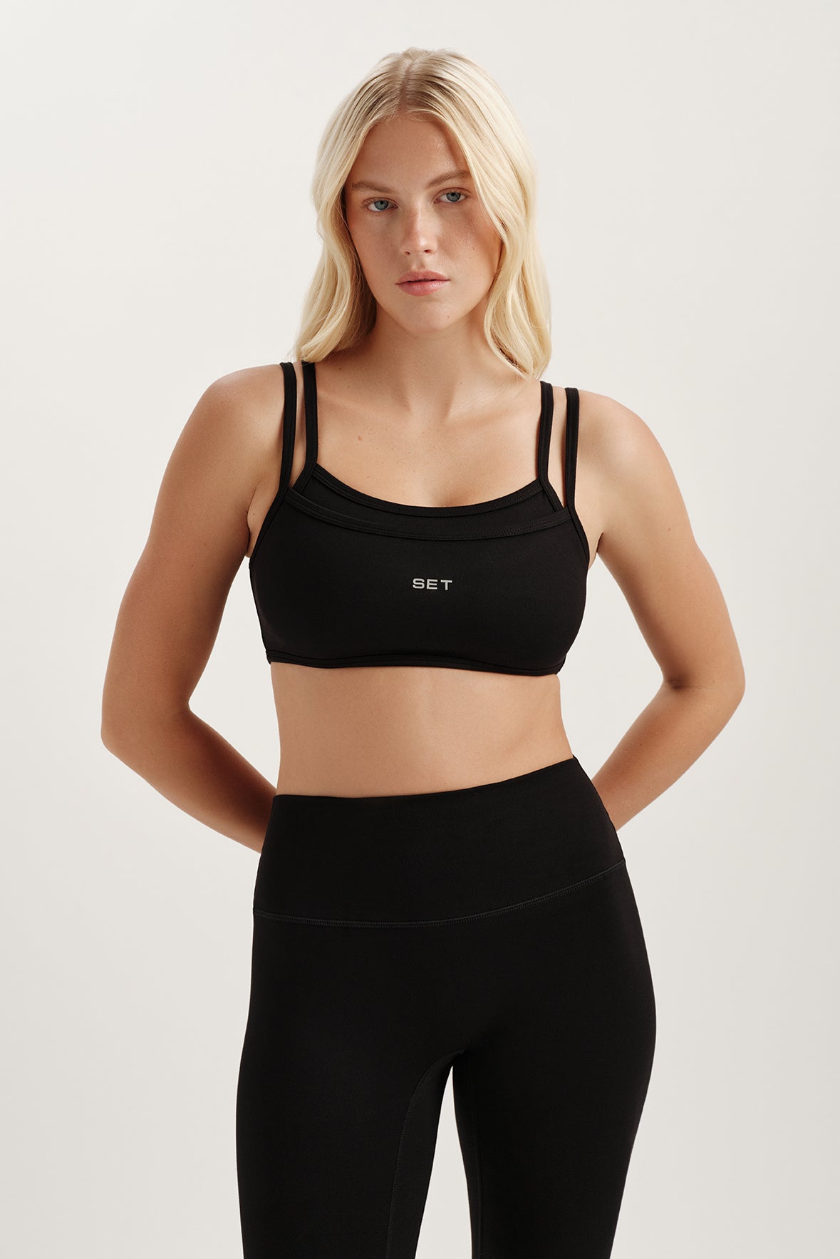Woman wearing a black sports bra and leggings with a visible brand logo on a light background <model-info>Kenzie wears a size S and is 5’6, 25” waist, 33” bust.</model-info>