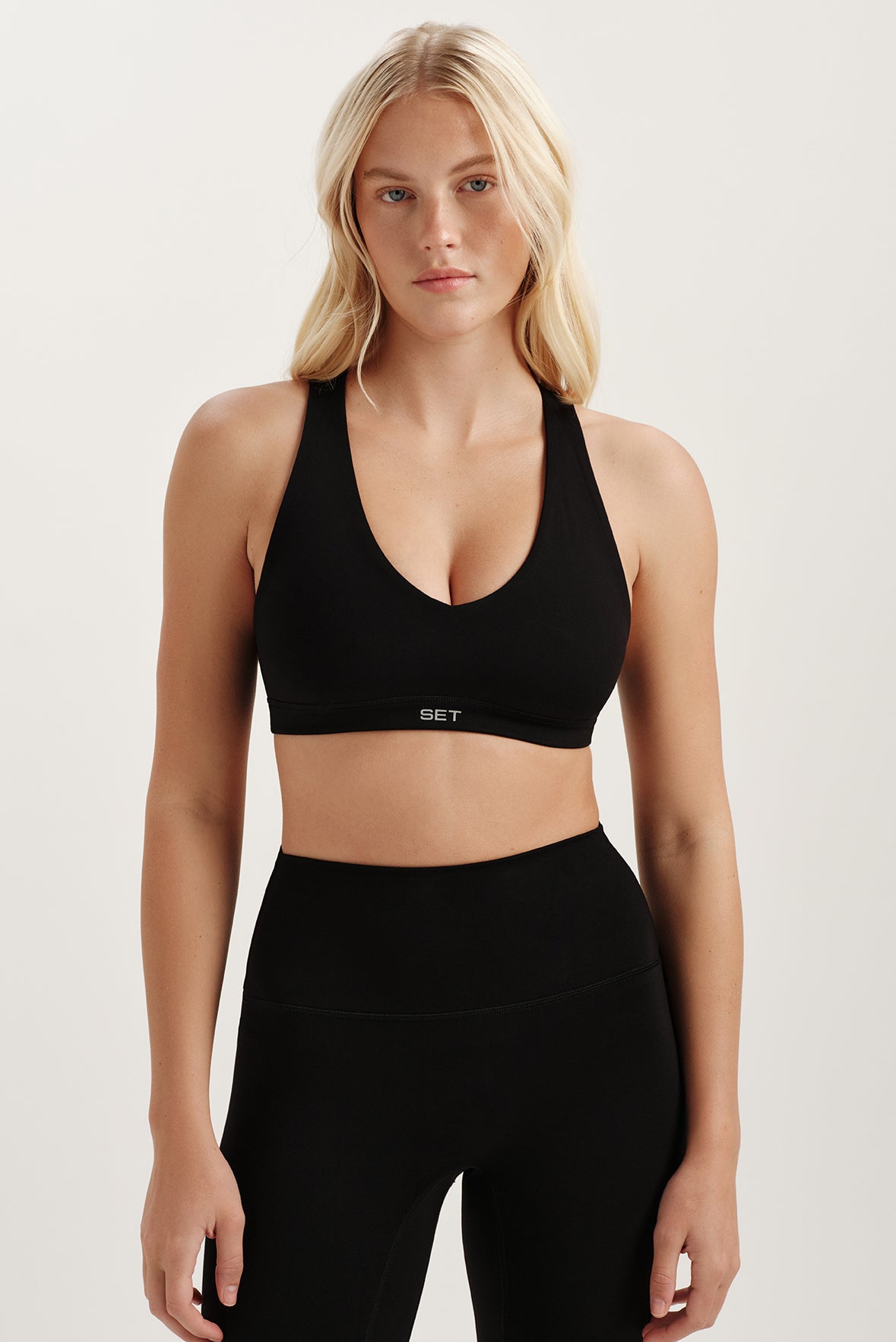 Woman wearing a black sports bra and leggings on a light background <model-info>Kenzie wears a size S and is 5’6, 25” waist, 33” bust.</model-info>