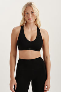 Woman wearing a black sports bra and leggings on a light background 
