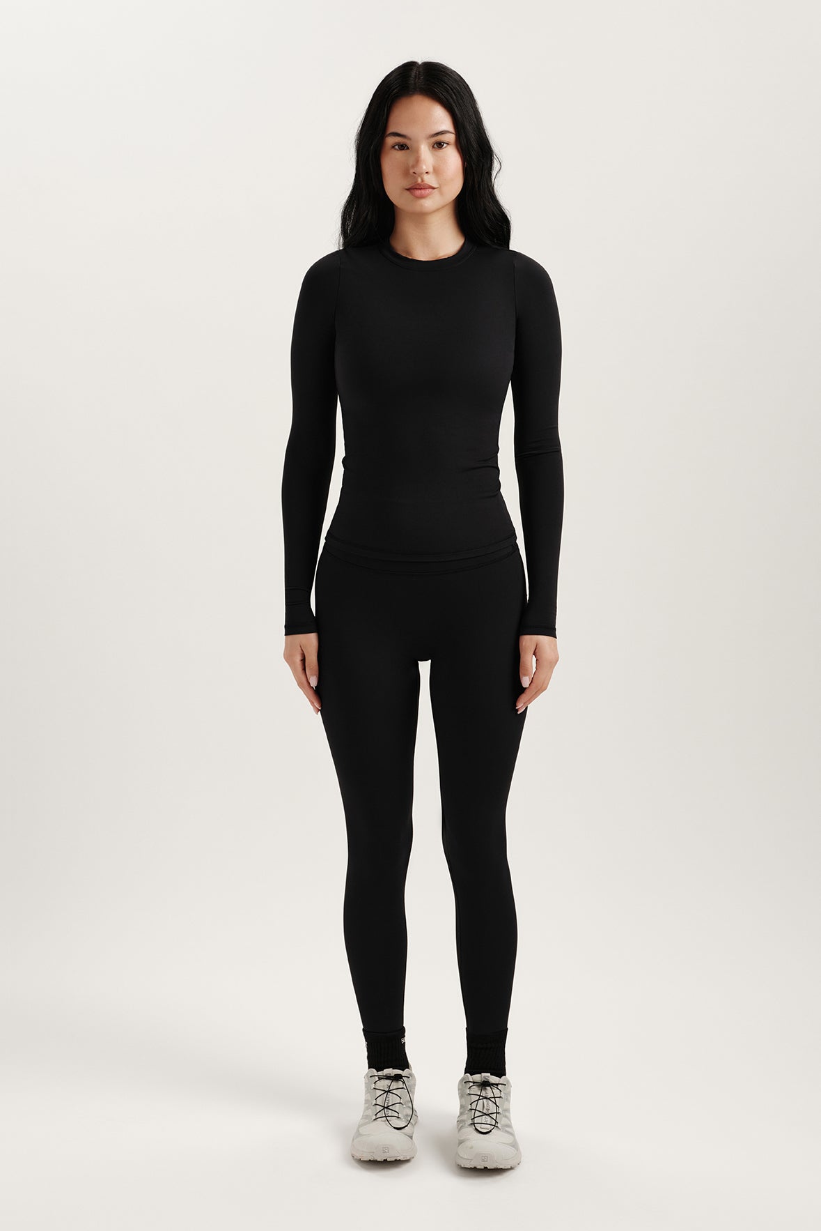 Person wearing a black long-sleeve top and leggings on a white background