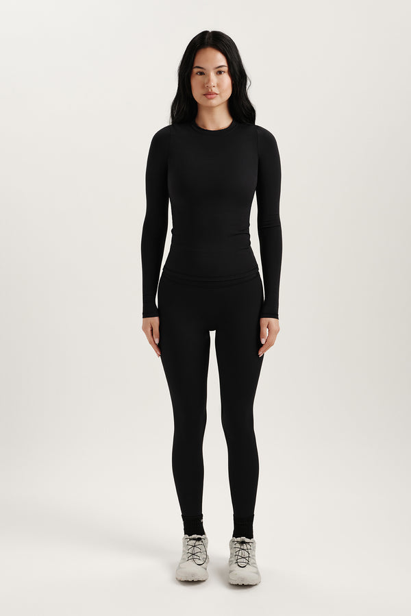 Person wearing a black long-sleeve top and leggings on a white background