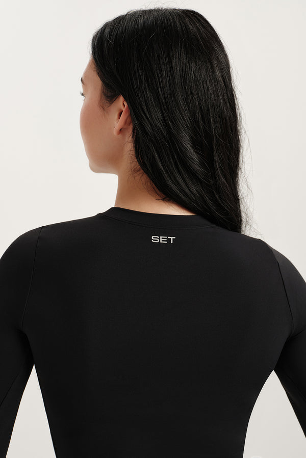 Person wearing a black long-sleeve shirt with 'SET' logo on the back against a white background