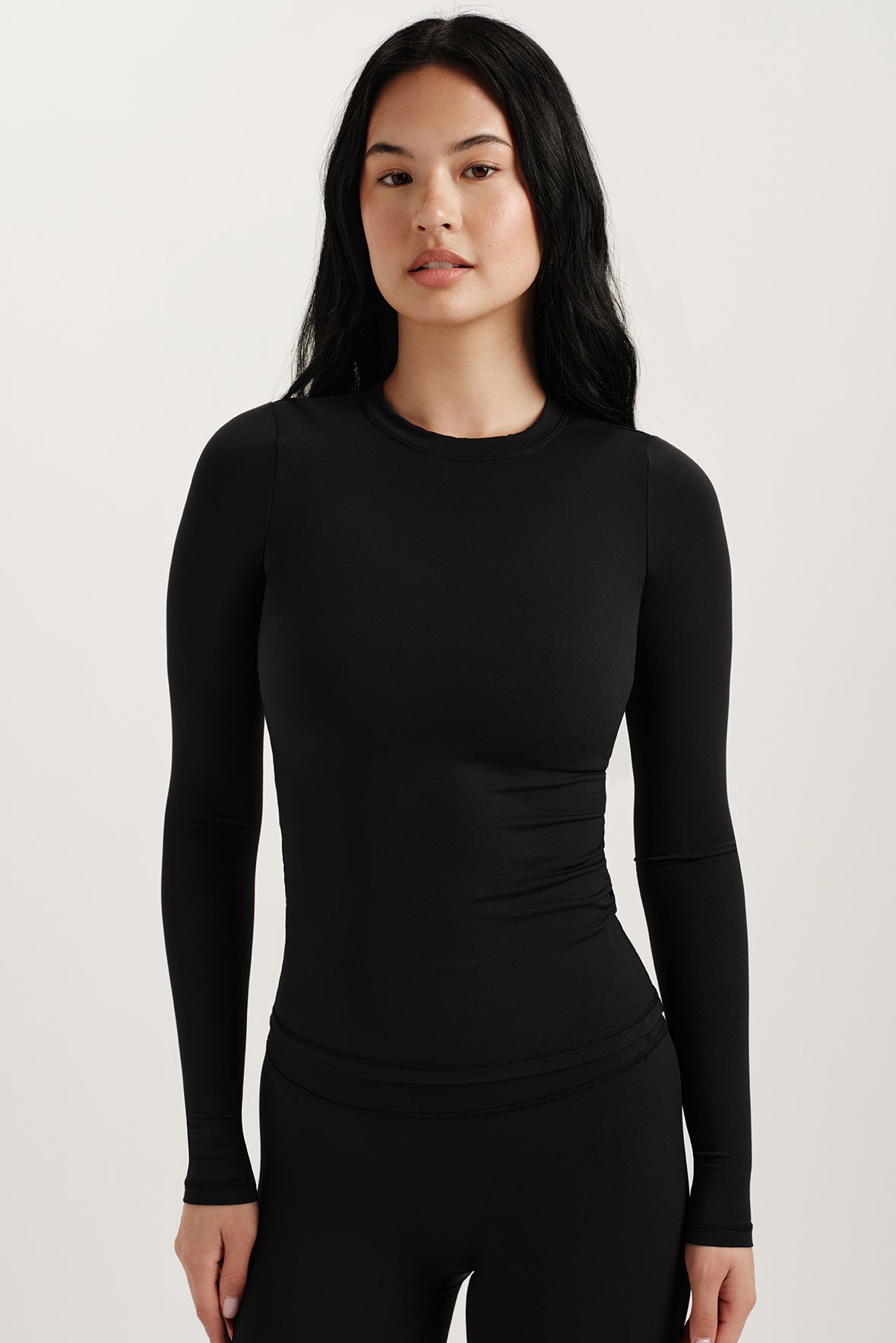 Woman wearing a black long-sleeve top against a plain background <model-info>Jasmine wears a size XS and is 5’8, 25” waist, 32C bust.</model-info> 
