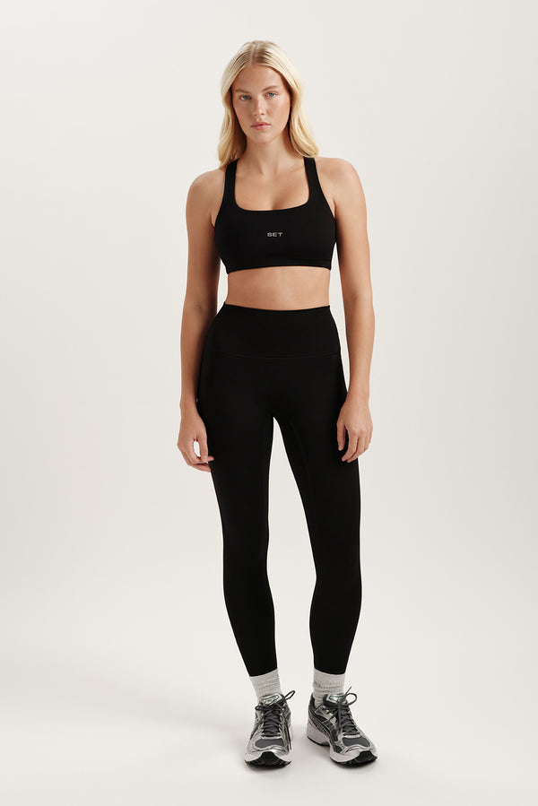 Woman wearing a black sports bra and leggings on a white background