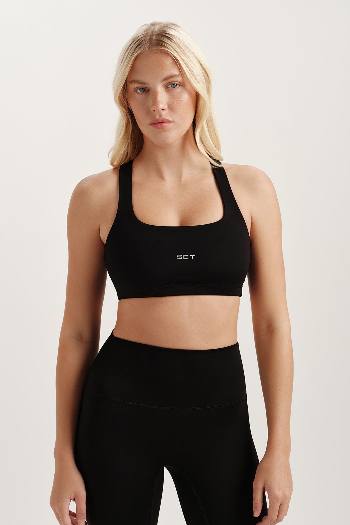 Woman wearing a black sports bra with 'SET' logo on a light background 