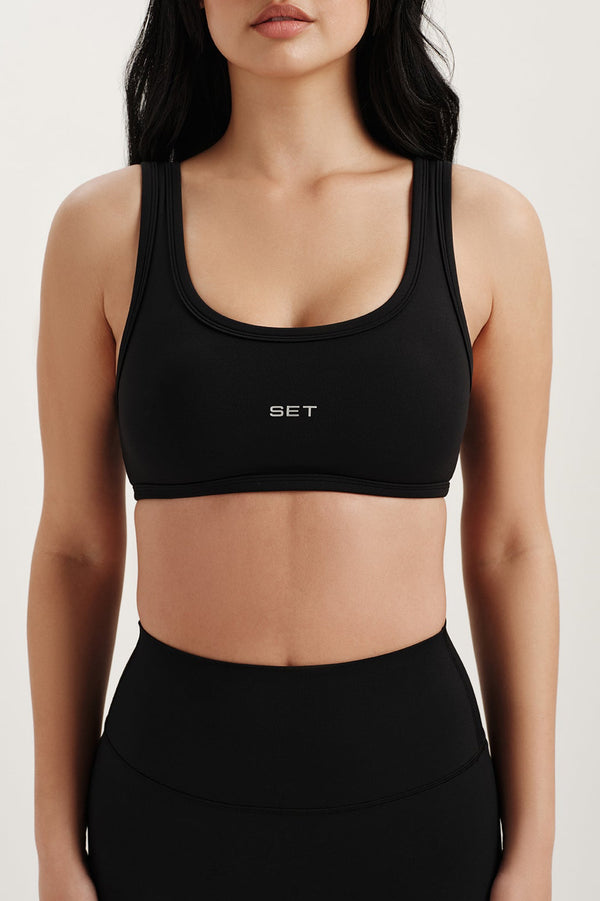 Woman wearing a black sports bra with 'SET' branding on a white background