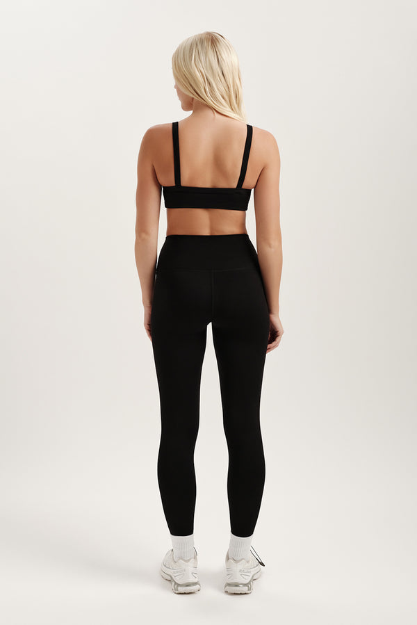 Person wearing a black sports bra and leggings set on a white background