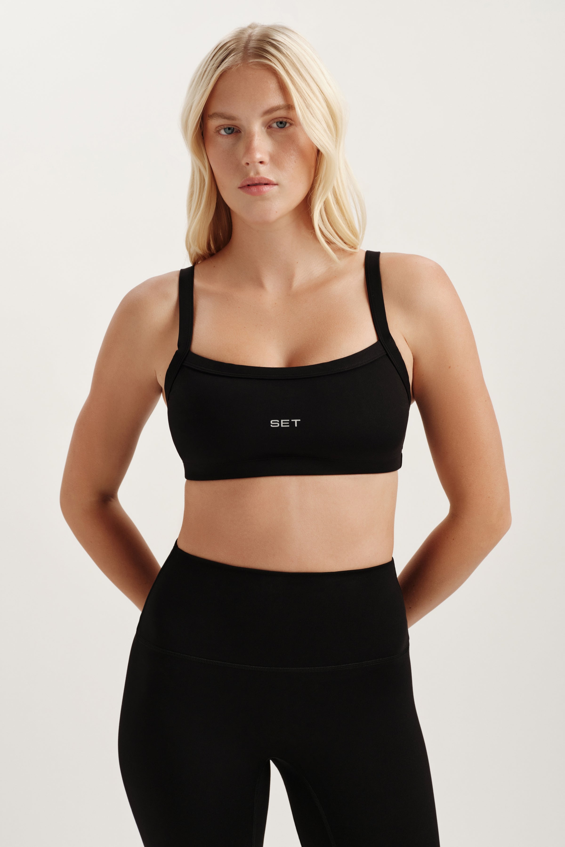 Woman wearing a black sports bra and leggings with a white background 