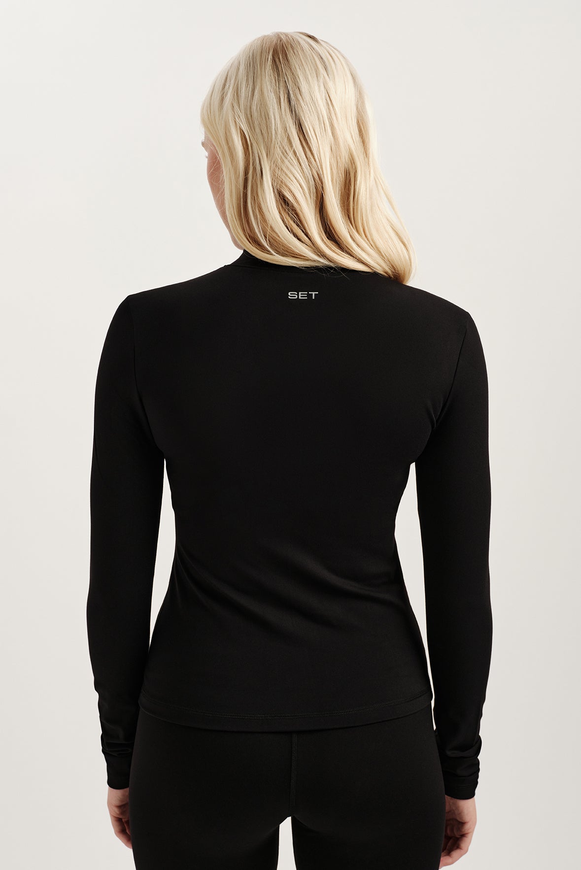 Person wearing a black long-sleeve top with 'SET' branding on the back against a light background