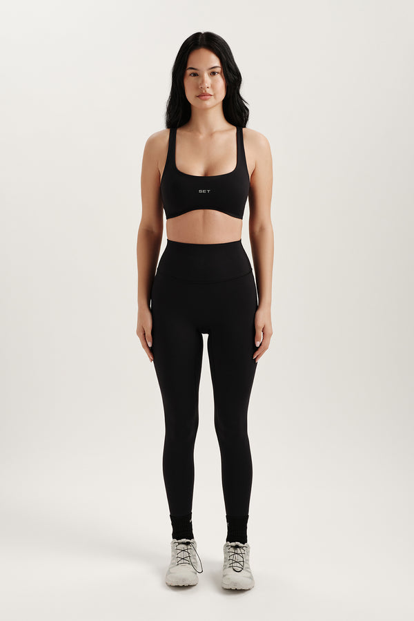 Woman wearing a black sports bra and leggings on a white background