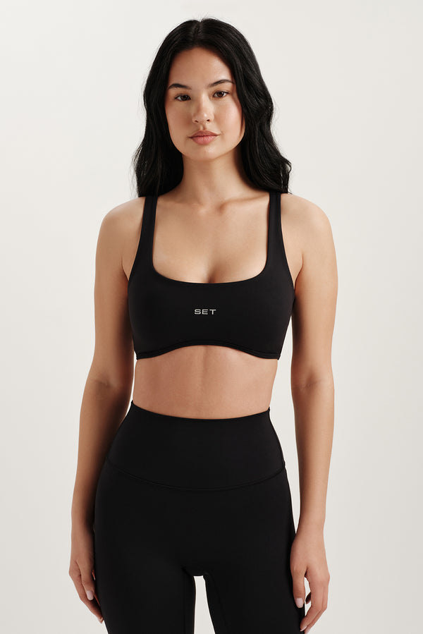 Woman wearing a black sports bra with 'SET' branding on a light background 