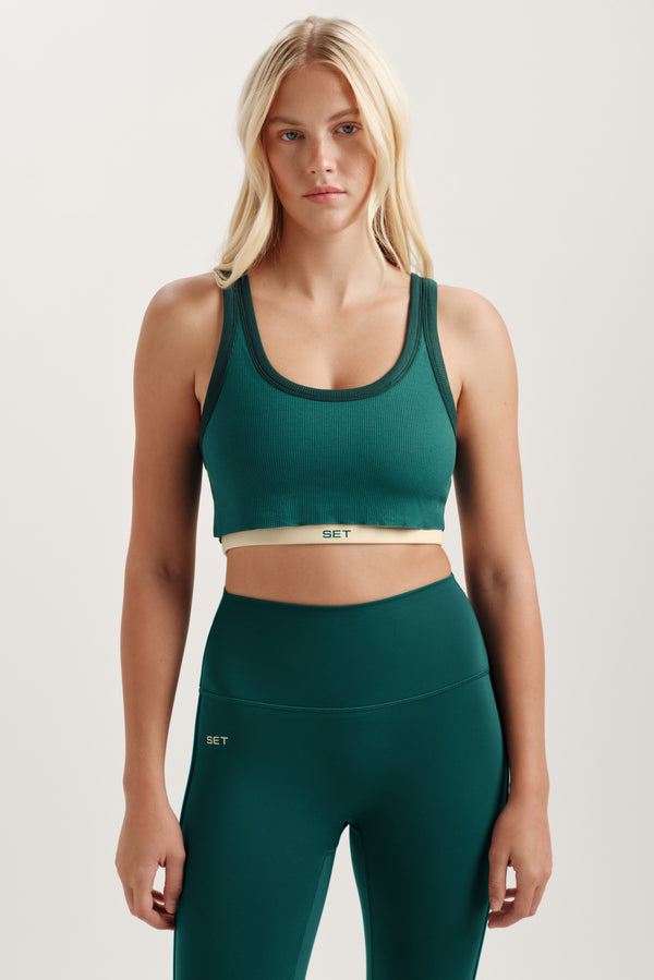 Woman wearing a green sports bra and leggings with a plain background 