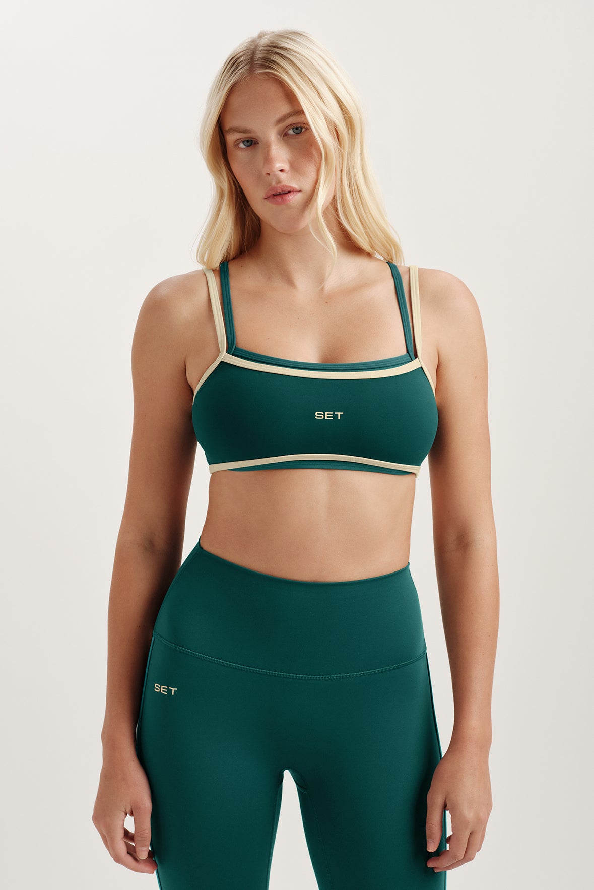 Woman wearing a green sports bra and leggings with 'SET' branding on a light background 