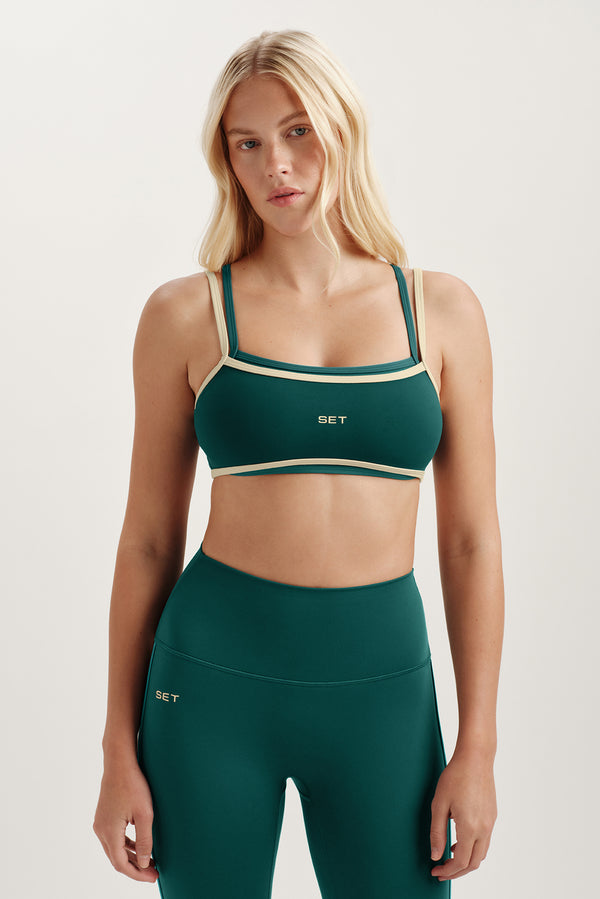 Woman wearing a green sports bra and leggings with 'SET' branding on a light background 