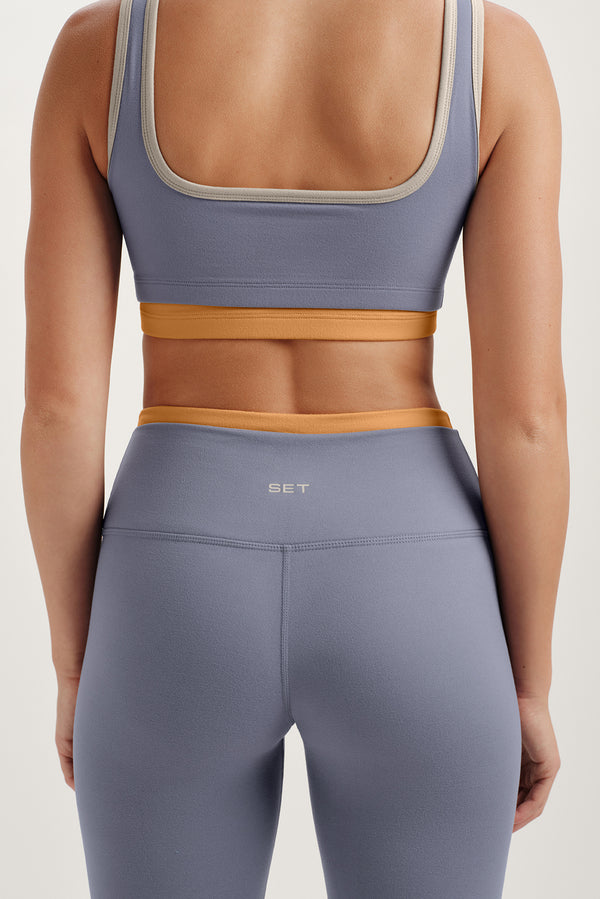 Person wearing a purple sports bra and leggings with a beige background