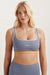 Woman wearing a purple sports bra with orange accents on a plain background <model-info>Kenzie wears a size S and is 5’6, 25” waist, 33” bust.</model-info> 