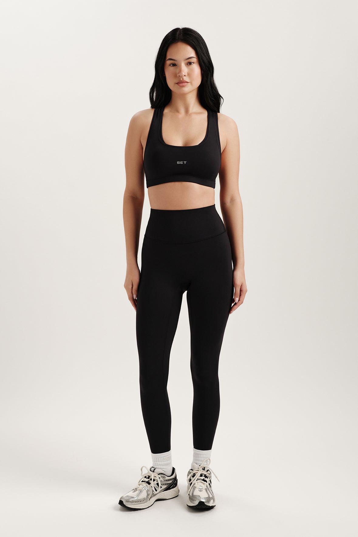 Woman wearing a black sports bra and leggings with a white background