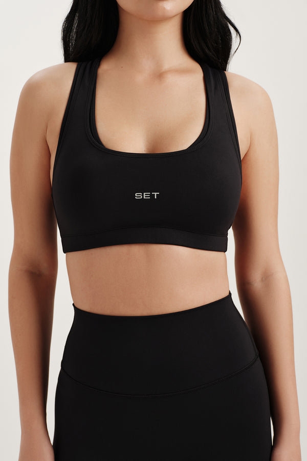 Person wearing a black sports bra with 'SET' logo on a white background