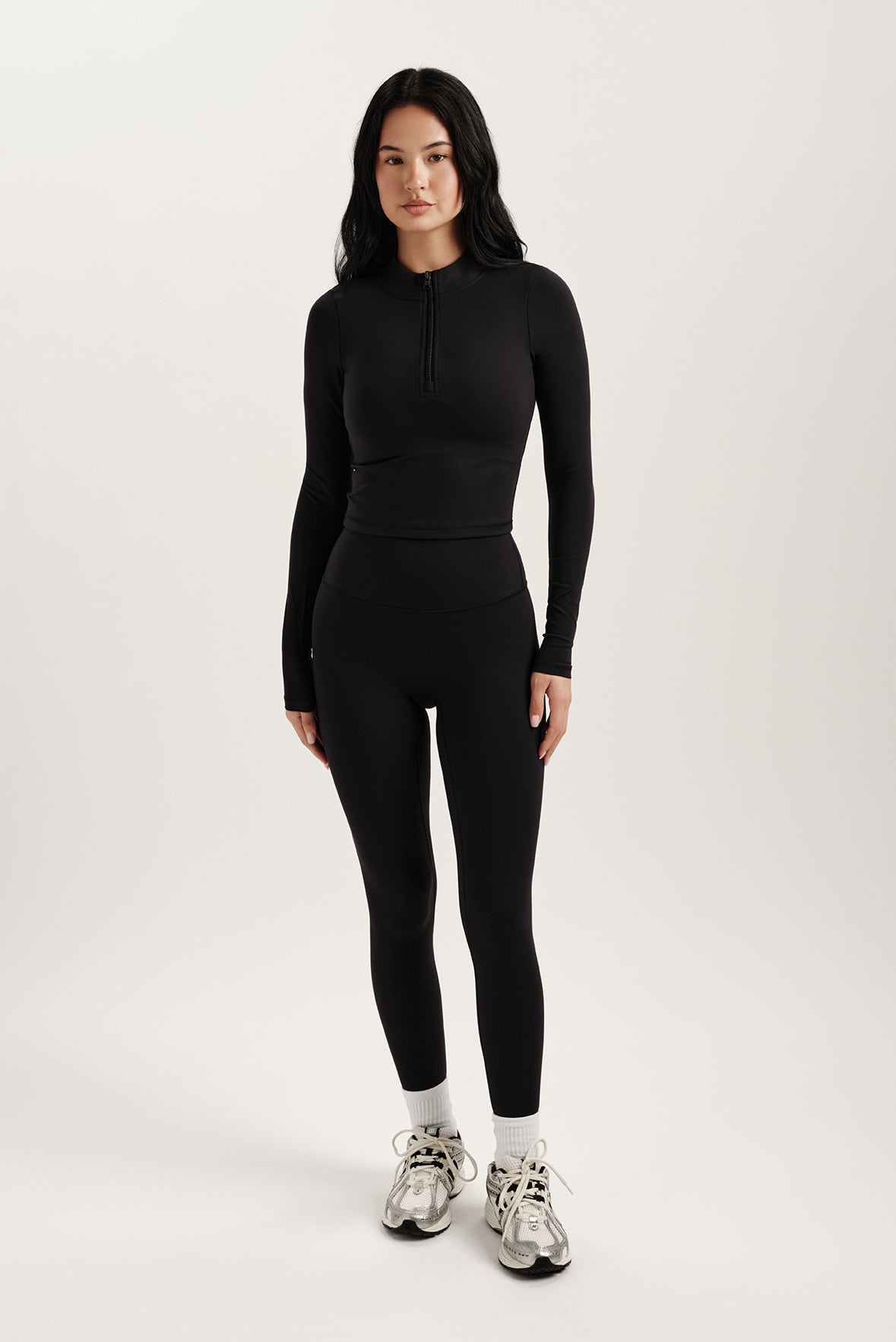 Woman wearing a black long-sleeve top and leggings on a white background