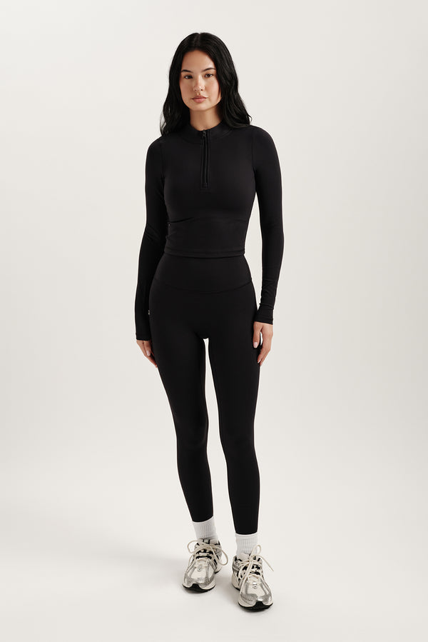 Woman wearing a black long-sleeve top and leggings on a white background