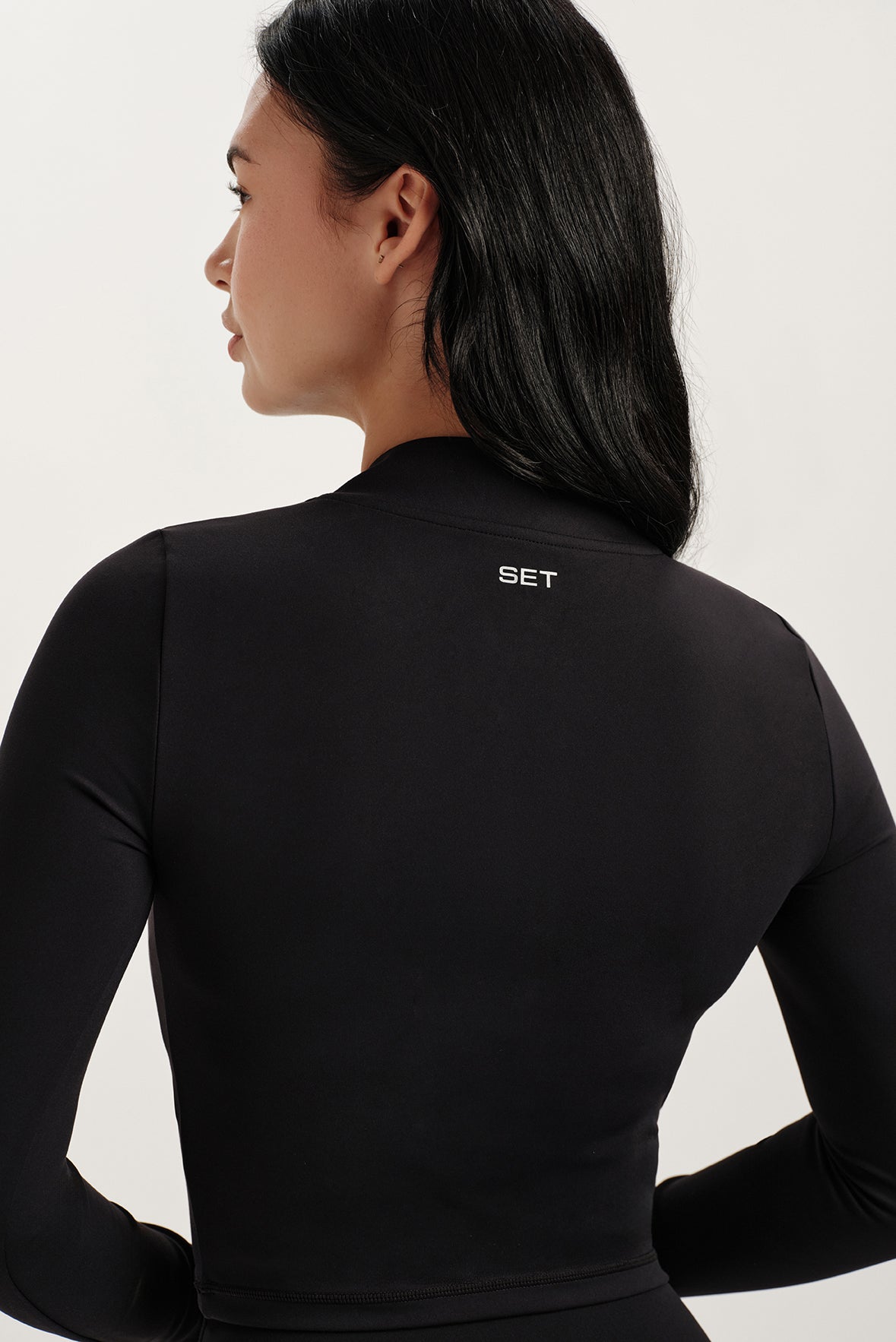 Person wearing a black long-sleeve top with 'SET' branding on the back against a white background
