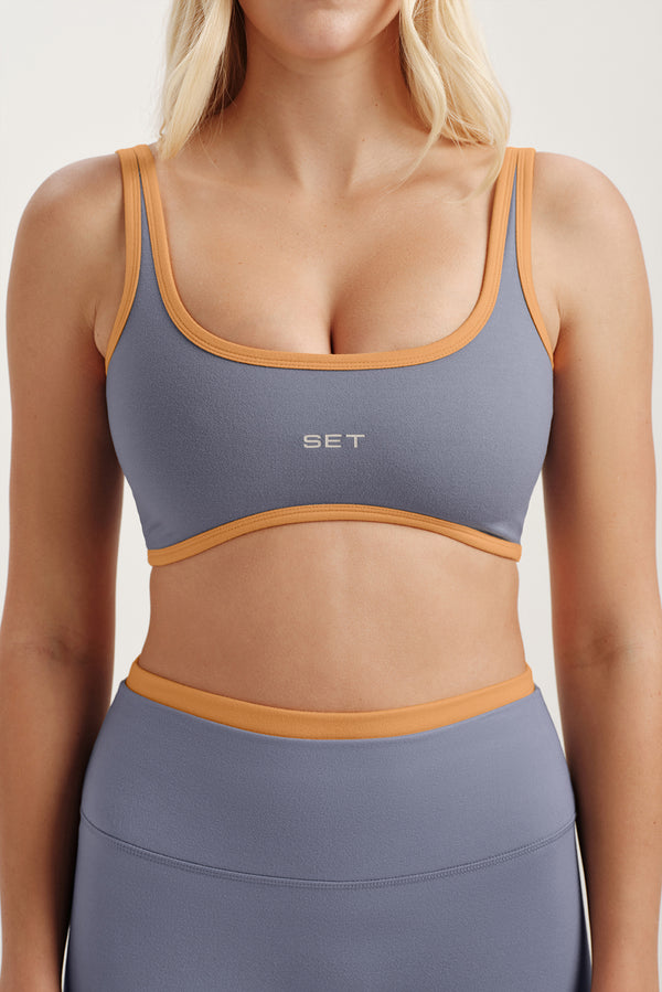 Purple sports bra with orange accents worn by a model on a plain background