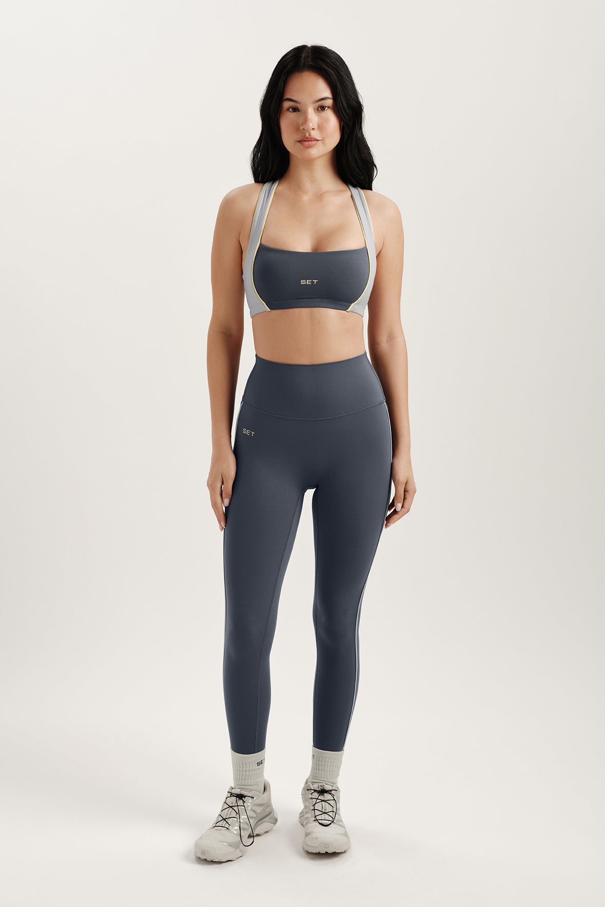 Woman wearing a gray sports bra and leggings set on a white background