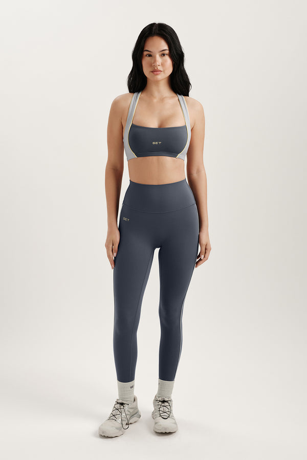 Woman wearing a gray sports bra and leggings set on a white background