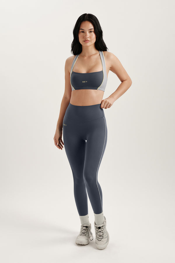 Woman standing in gray sports bra and gray leggings on a white background 