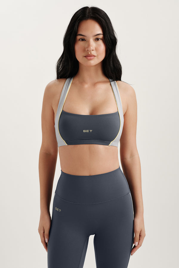 Woman wearing a gray sports bra and leggings with a white background 