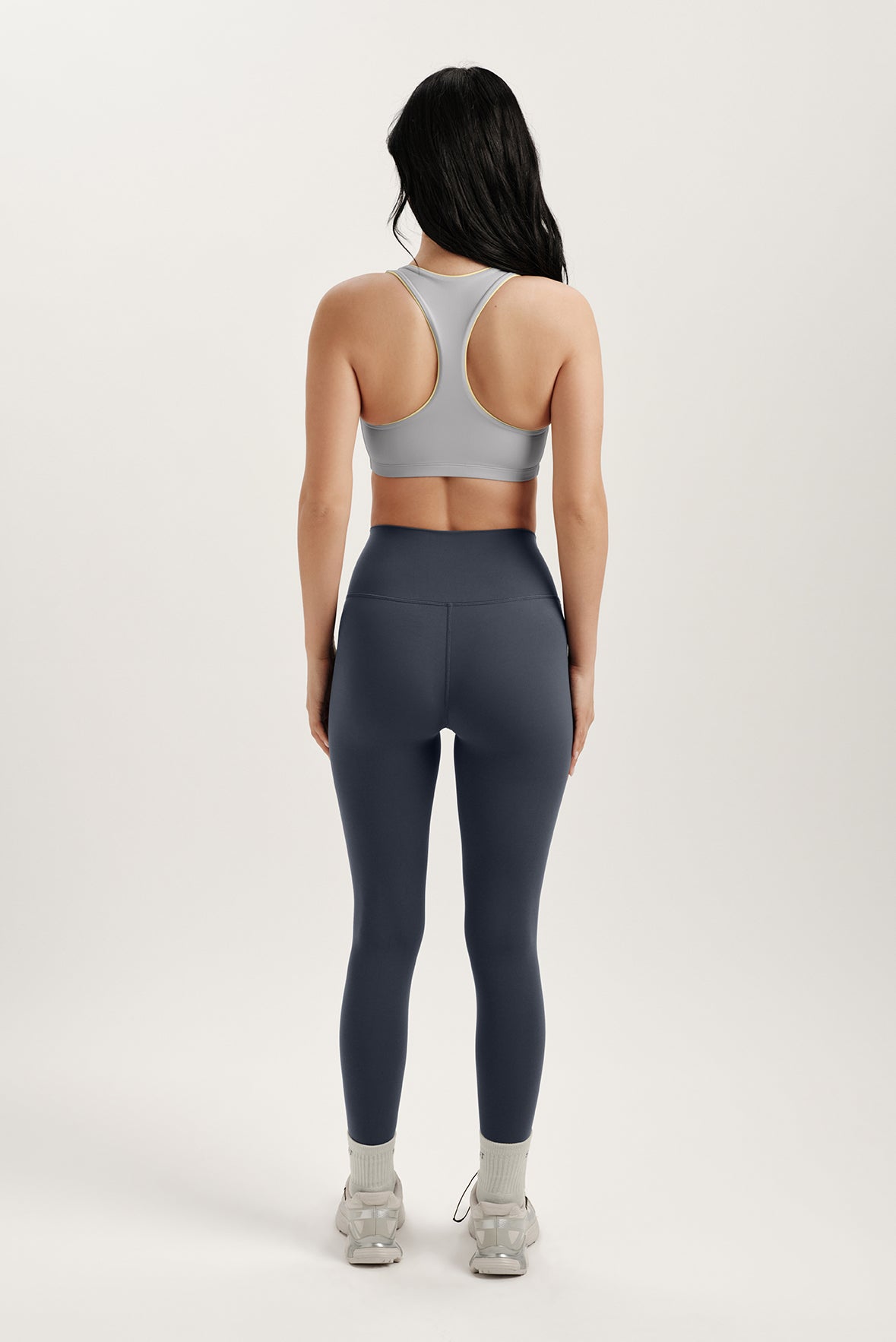 Person wearing a gray sports bra and dark gray leggings on a white background