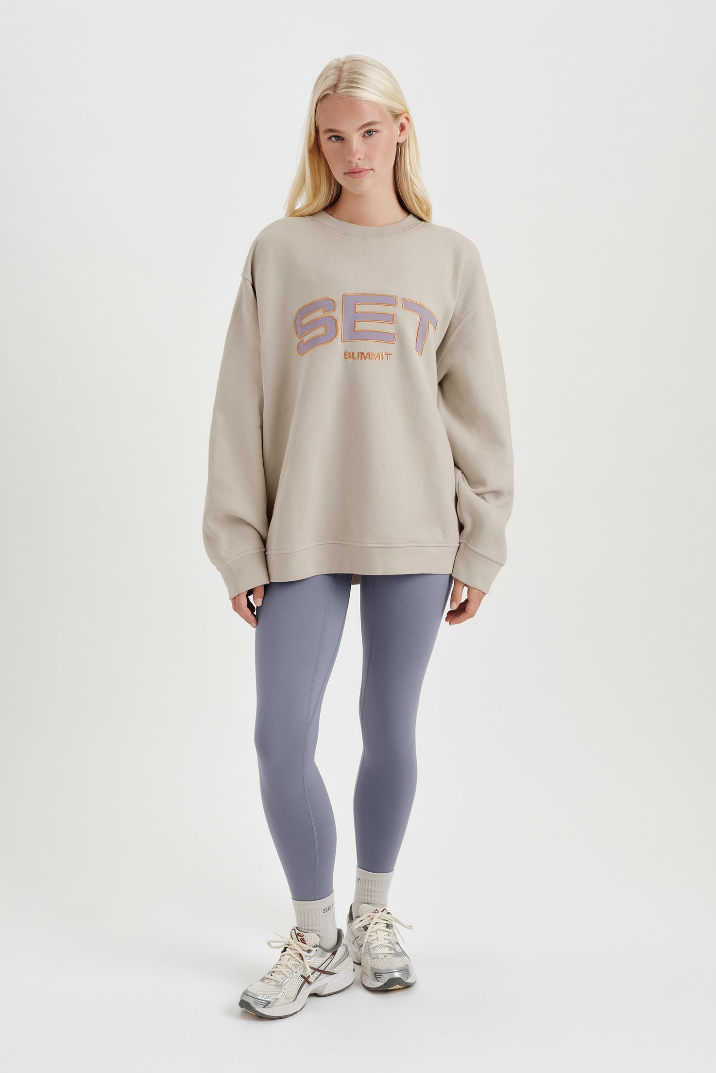 Woman wearing a beige sweatshirt with colorful text and leggings on a white background