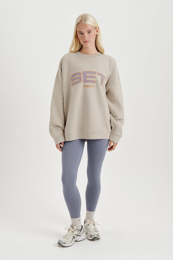 Woman wearing a beige sweatshirt with colorful text and leggings on a white background