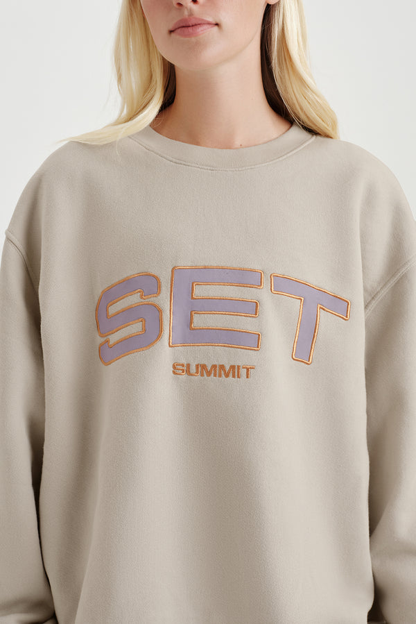 Beige sweatshirt with 'SET SUMMIT' text worn by a person