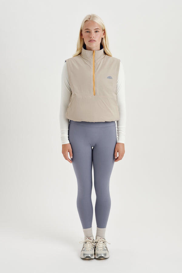 Woman wearing a beige insulated vest and gray leggings on a white background