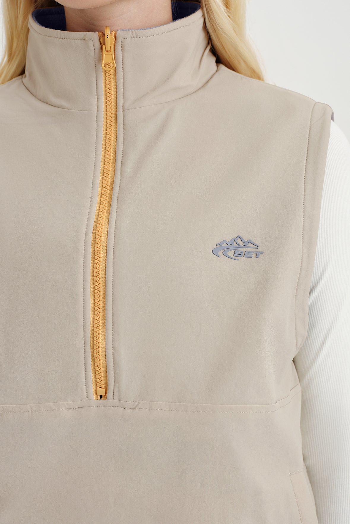 Beige vest with a yellow zipper and logo on a white background